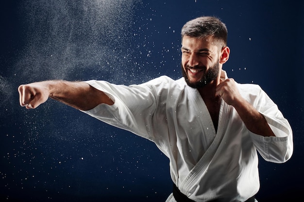 Hombre de karate en un kimono golpea una mano sobre fondo azul.