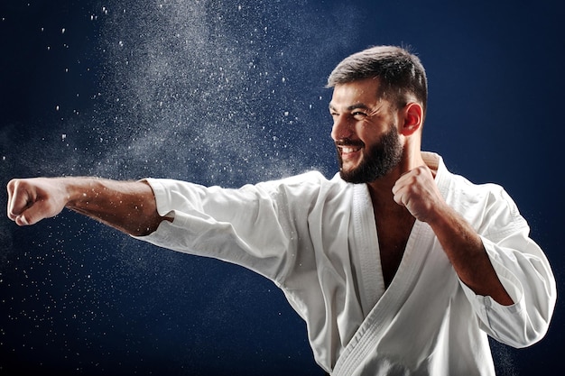 Hombre de karate en un kimono golpea una mano sobre fondo azul.