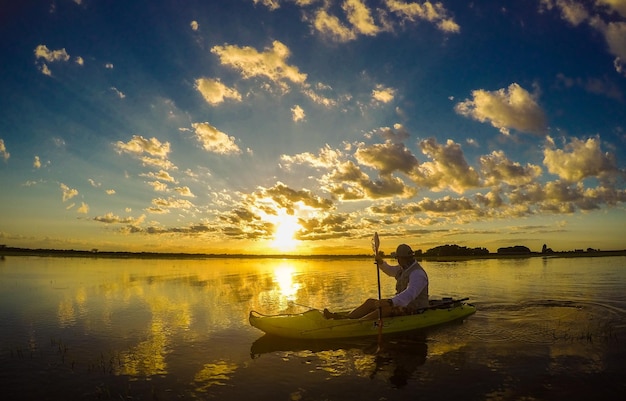 Hombre en kayak en el lago contra el cielo nublado durante la puesta de sol