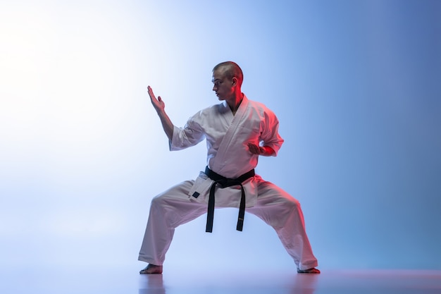 Hombre en kimono blanco y cinturón negro de entrenamiento de karate sobre fondo blanco.