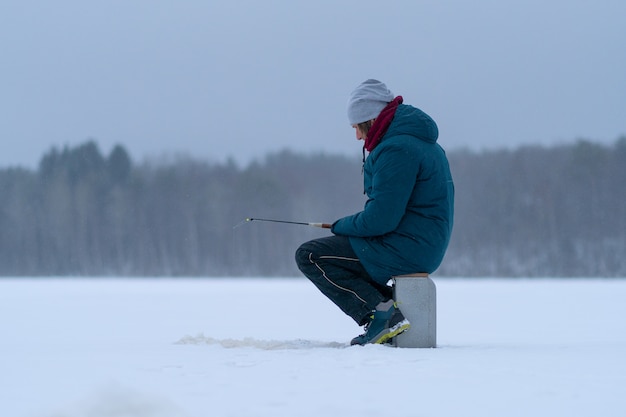 Un hombre en un lago nevado congelado. Vista lateral. Pesca de invierno