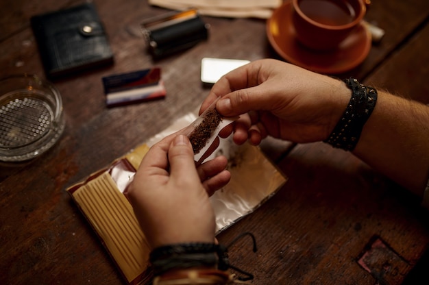 El hombre lanza un cigarrillo, mesa de madera en el fondo. Cultura de fumar tabaco, sabor rico específico. Ocios de fumador masculino en Office