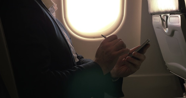 Hombre con lápiz para escribir en el teléfono inteligente en el avión