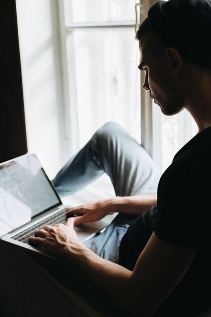 Hombre con laptop en el alféizar de la ventana