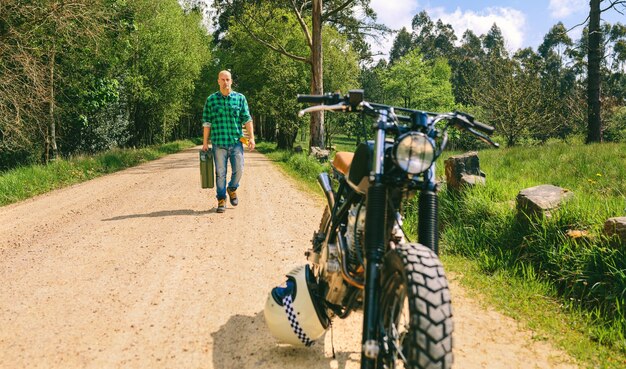 Hombre con lata de gasolina caminando hacia una moto vintage personalizada