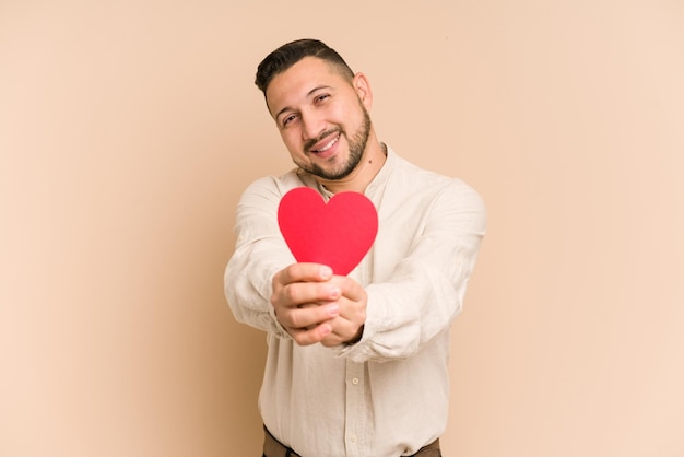 Hombre latino adulto sosteniendo un concepto de día de san valentín de corazón de papel aislado