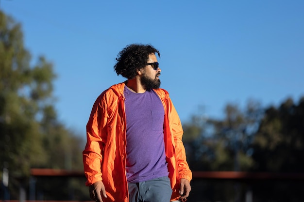 hombre latino con barba y cabello rizado en un parque mirando a un lado