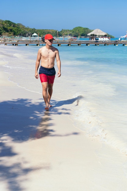Hombre latino caminando por la playa con una gorra en la cabeza
