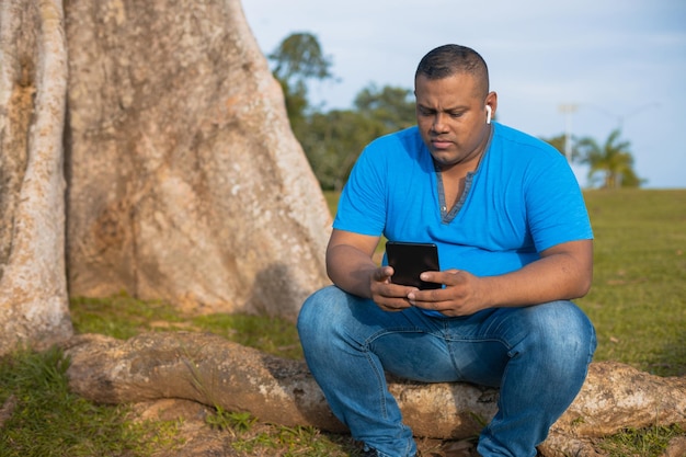 Hombre latino charlando con su celular en el árbol