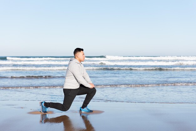 Hombre latino estirando el músculo psoas en la playa