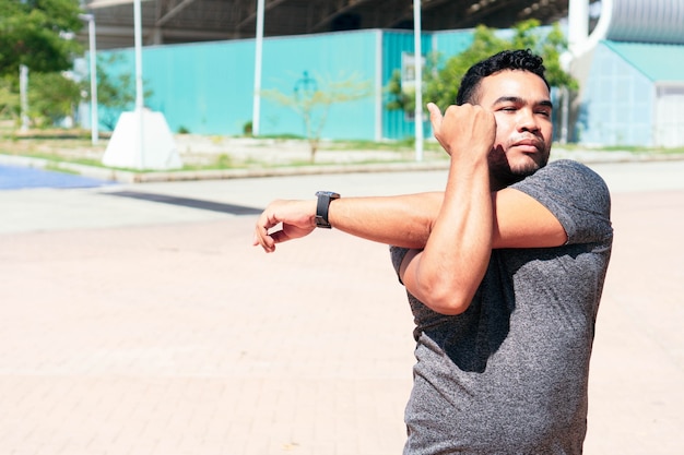 Hombre latino estirando su brazo y calentando para entrenar.