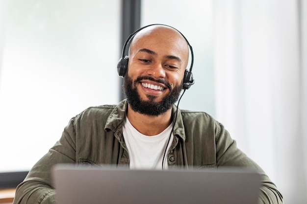Hombre latino feliz con barba en auriculares mirando la computadora portátil y sonriendo con videollamada desde casa