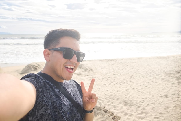 Hombre latino feliz en la playa haciendo el signo de la victoria con copyspace