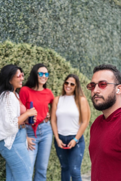 Hombre latino con gafas de sol mirando hacia otro lado cerca de amigos