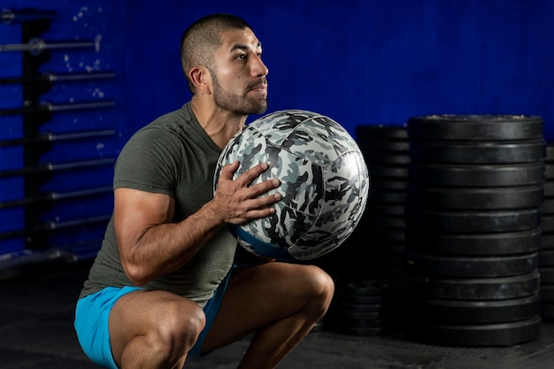 Hombre latino haciendo ejercicio en un gimnasio usando un balón medicinal crossfit