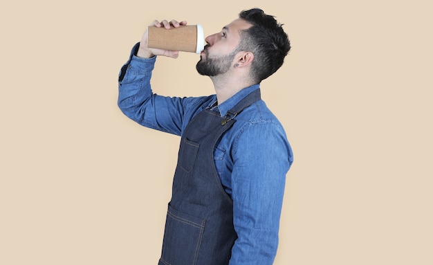 Hombre latino hispano con delantal y camisa está de perfil sobre fondo amarillo mientras bebe un café