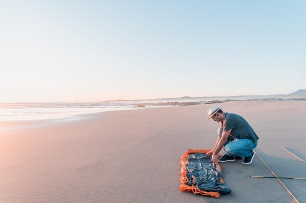 El hombre latino instaló o mantuvo una carpa en la playa solo al acampar al atardecer