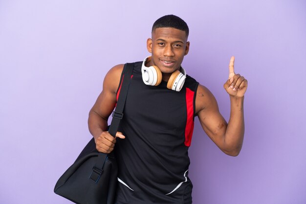 Hombre latino joven deporte con bolsa de deporte aislado en púrpura apuntando hacia una gran idea