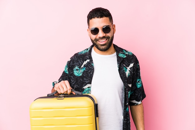 Hombre latino joven que sostiene una maleta feliz, sonriente y alegre.