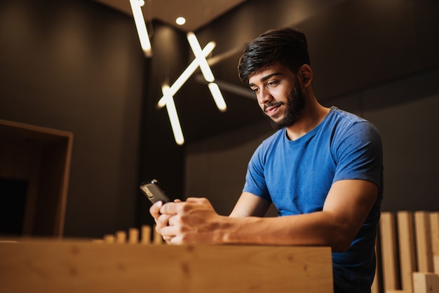 Hombre latino joven que usa el teléfono celular. Mensajes de texto en la cafetería.