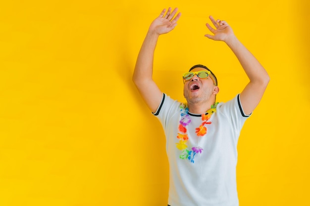 Foto hombre latino levantando las manos y gritando porque ganó usando gafas de sol y un collar de flores