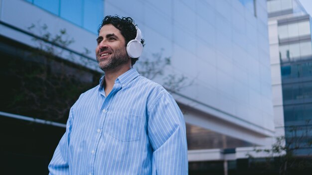 Hombre latino de mediana edad con auriculares inalámbricos camina por las calles sonriendo espacio de copia