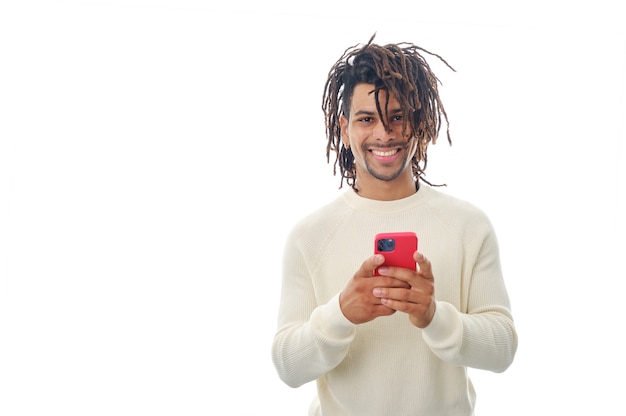 Foto hombre latino mirando a la cámara y sonriendo mientras sostiene un teléfono móvil sobre un fondo aislado.