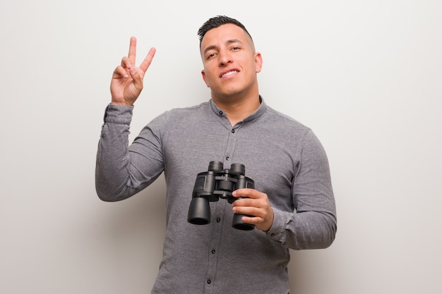 Hombre latino que muestra el número dos. Él está sosteniendo unos binoculares.