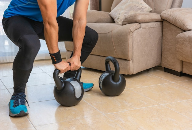 Hombre latino que realiza un entrenamiento de cross fit en casa con un par de pesas rusas.