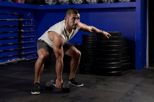 Hombre latino con ropa deportiva haciendo ejercicios con pesas en el gimnasio.