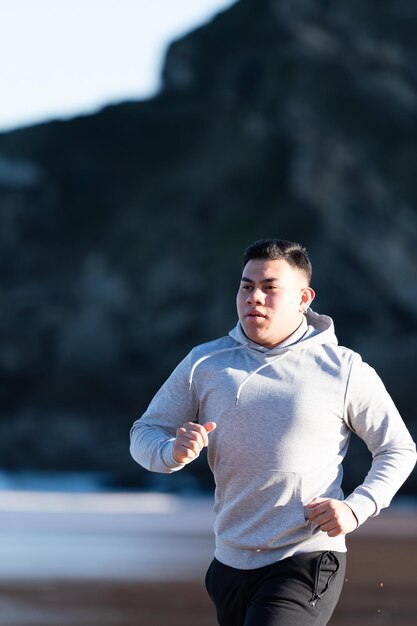 Hombre latino con sobrepeso corriendo en la playa