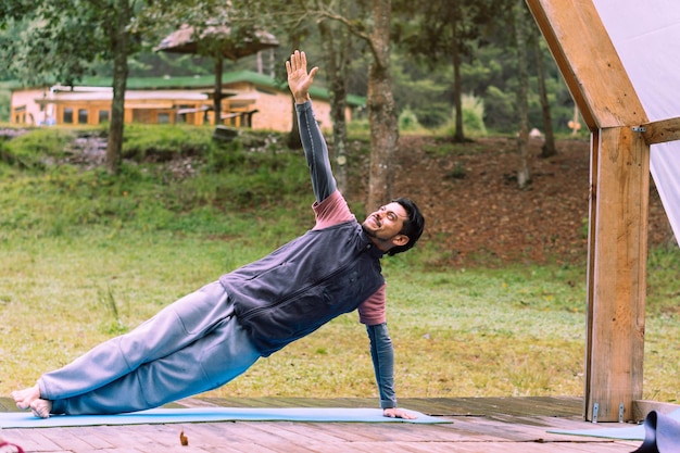 Hombre latino sonriendo y practicando yoga en un bosque.