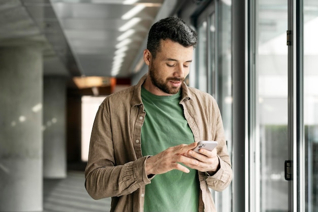Hombre latino sosteniendo un teléfono móvil leyendo un mensaje de texto Hipster usando una aplicación móvil comprando en línea