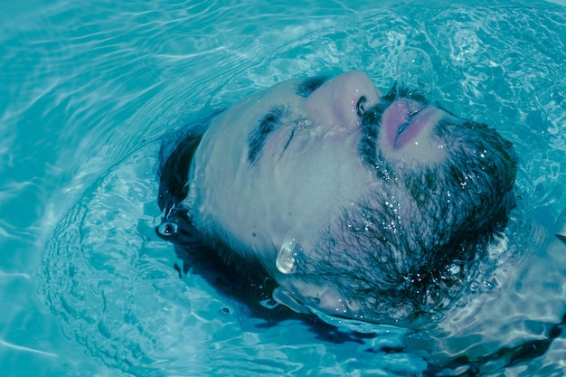 Hombre latino sumergido en agua sacándose la cara ahogándose lucha contra el agua