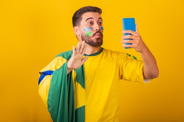 Hombre latinoamericano brasileño animando a brasil en la copa del mundo 2022 en videollamada hablando con amigos de forma remota teléfono celular con tecnología de comunicación celular