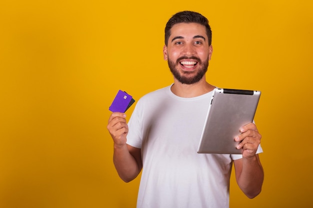 Hombre latinoamericano brasileño sorprendido y feliz sosteniendo una tableta y una tarjeta de crédito haciendo compras a través de una aplicación o Internet