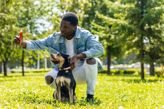 Hombre latinoamericano caminando con su lindo perro en un día soleado en el césped del parque de la ciudad en el césped