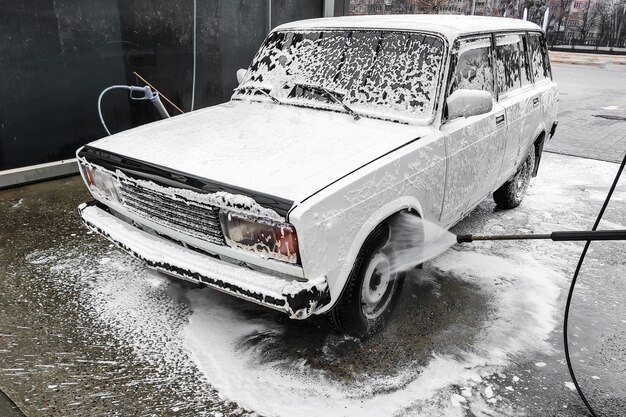 Un hombre lava un auto blanco. La espuma de lavado especial elimina la suciedad.