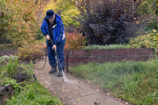 Un hombre lava un camino de jardín con una hidrolimpiadora de alta presión. Trabajo de otoño en el jardín.
