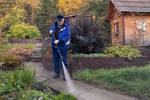 Un hombre lava un camino de jardín con una hidrolimpiadora de alta presión. Trabajo de otoño en el jardín.