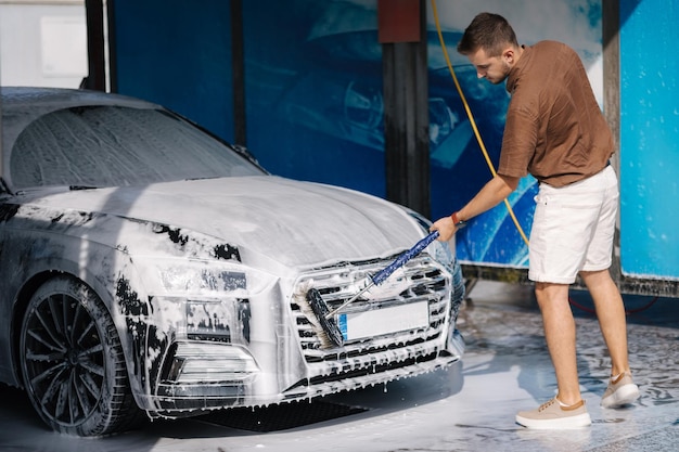 Un hombre lava un coche con un cepillo especial en un lavado de coches un conductor masculino lava la parrilla del radiador