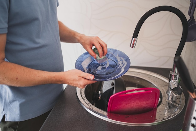 Un hombre lava platos con una esponja una persona lava el detergente con agua de los platos cerca ...