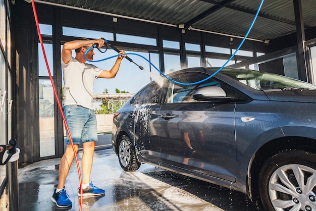 Un hombre lava su auto en un autolavado de autos usando una manguera con agua a presión