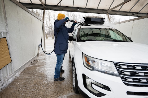 Hombre lavando agua a alta presión coche todoterreno americano con portaequipajes en lavado de autoservicio en clima frío