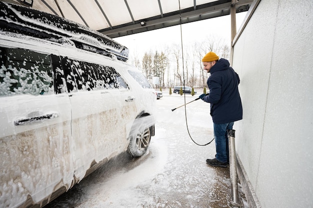 Hombre lavando agua a alta presión coche todoterreno americano con portaequipajes en lavado de autoservicio en clima frío