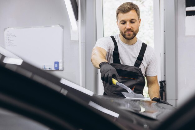 Hombre lavando el capó del automóvil y preparando el proceso de pulido del revestimiento del vidrio del automóvil Trabajador masculino instalando película de protección en el automóvil en el garaje Detallado del automóvil