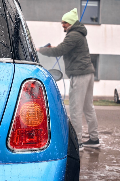 Un hombre lavando su auto bajo la lluvia.