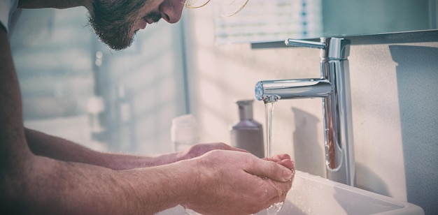 Hombre lavándose la cara con agua en el baño.