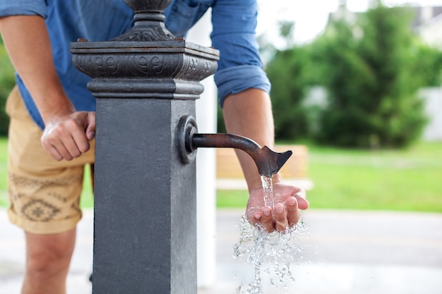 Hombre lavándose las manos en el agua del grifo en el parque