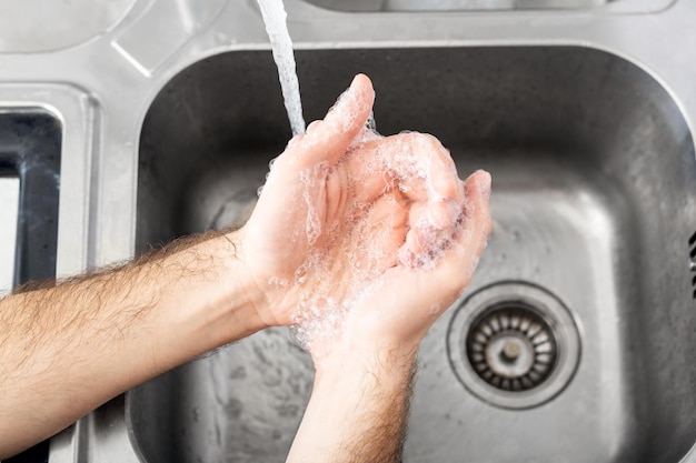 Hombre lavándose las manos con agua y jabón antibacteriano en el fregadero de metal para la prevención del virus corona. Higiene de manos, salud, concepto médico. La desinfección de la piel de las manos protege del coronavirus covid 19.